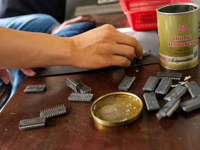 Hands sanding and re-marking electronic components next to a tin can of supplies.
