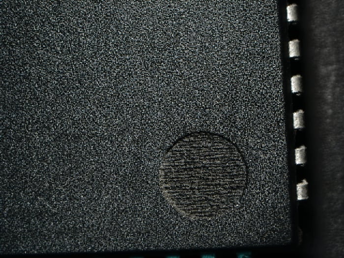 Counterfeit UPD70320L-8 with a circle etched to fake a molded indent, visible under microscope