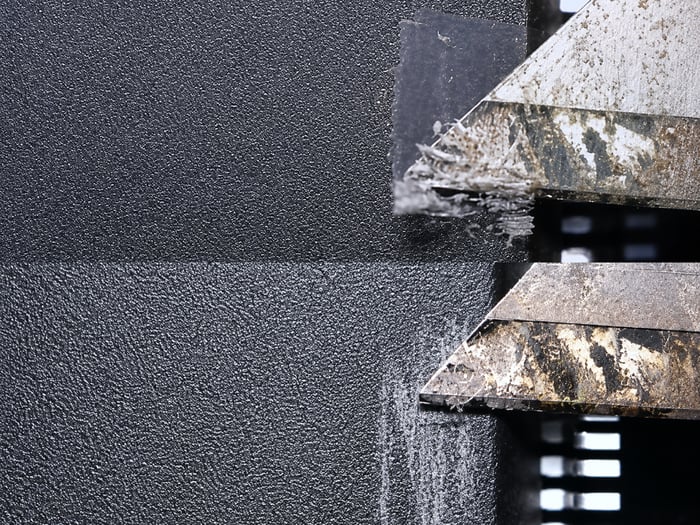 Blade scraping a blacktopping coating off a counterfeit part, top side coated and bottom side bare